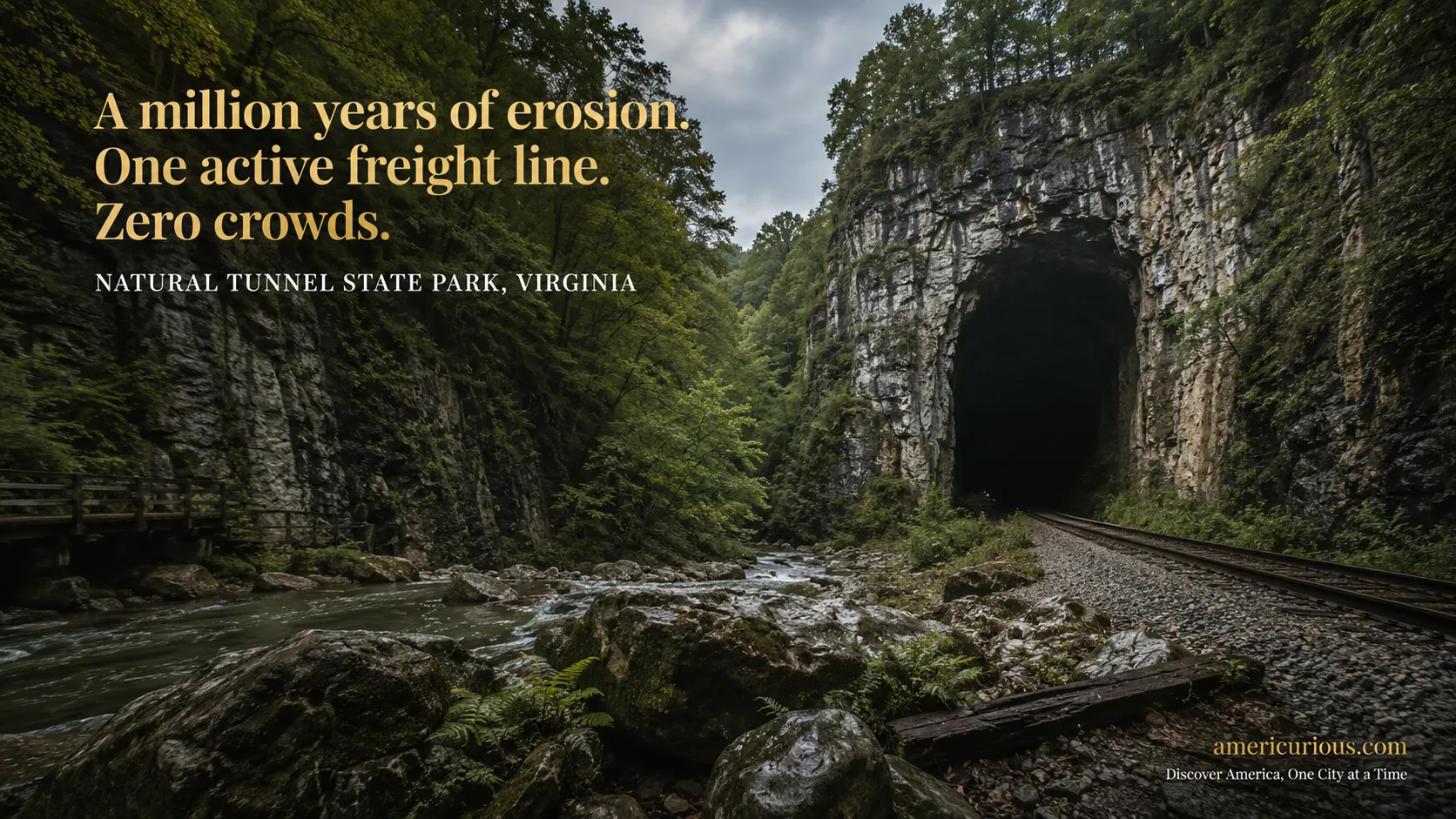 Cinematic wide-angle view of Natural Tunnel State Park, Virginia — a massive Ordovician limestone tunnel mouth opening through a forested Appalachian gorge with active railroad tracks at Stock Creek level — americurious.com guide to underrated Virginia state parks